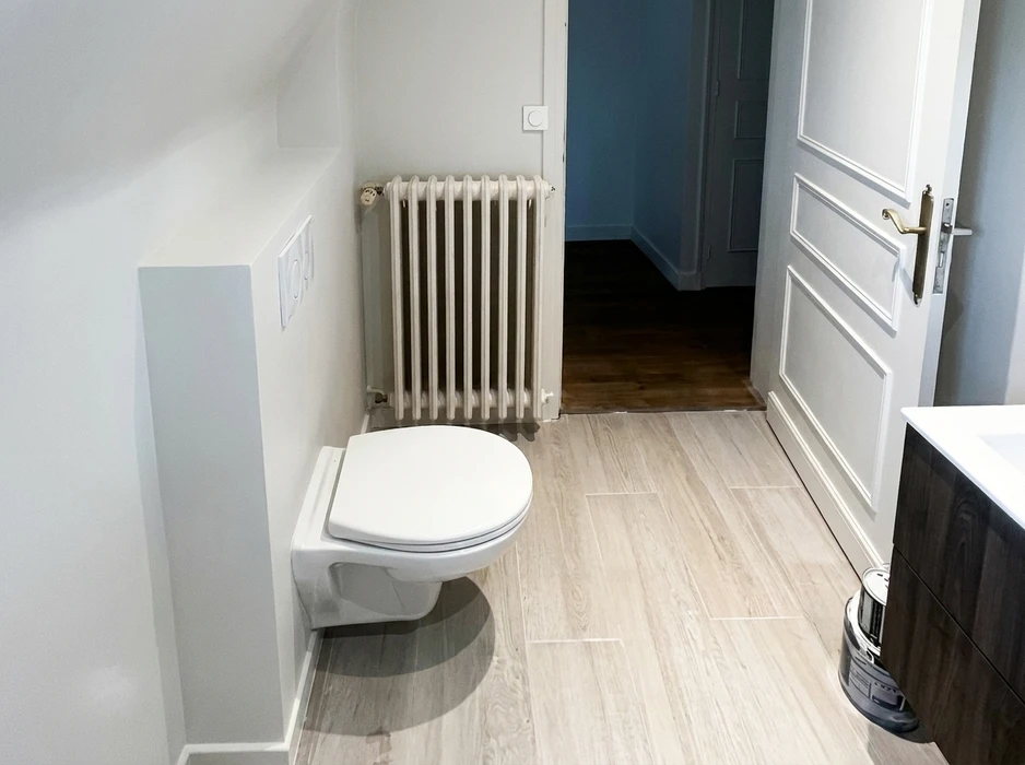 Salle de bains rénovée avec WC suspendu blanc fixé sur bâti-support encastré, carrelage imitation parquet en grès cérame clair