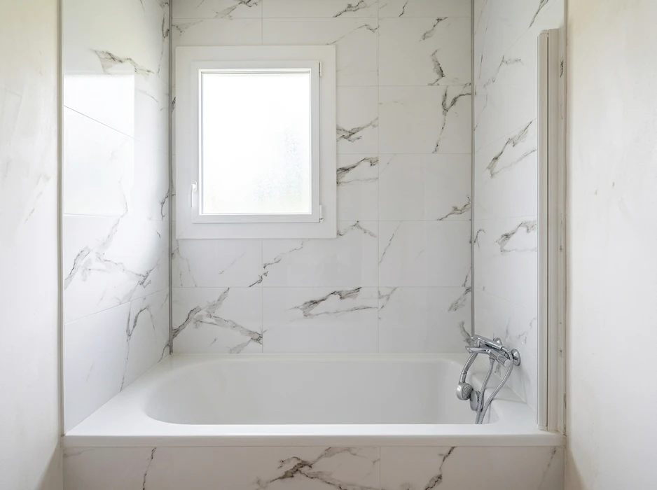 Salle de bain moderne avec baignoire encastrée blanche, habillage mural en carrelage grand format effet marbre Calacatta blanc veiné gris