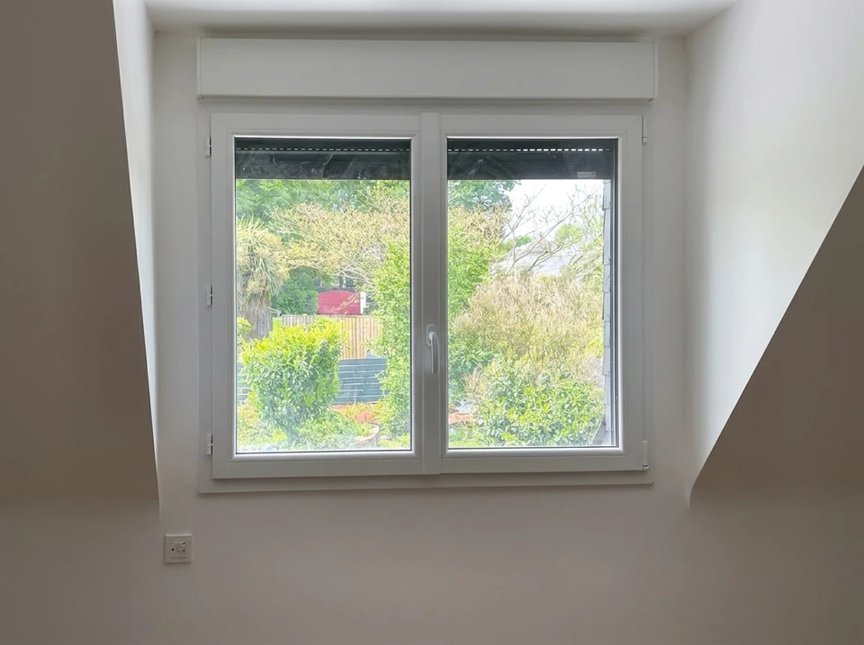 Deux ouvriers en salopettes bleues et casquettes blanches installent une fenêtre PVC dans un intérieur résidentiel aux murs blancs