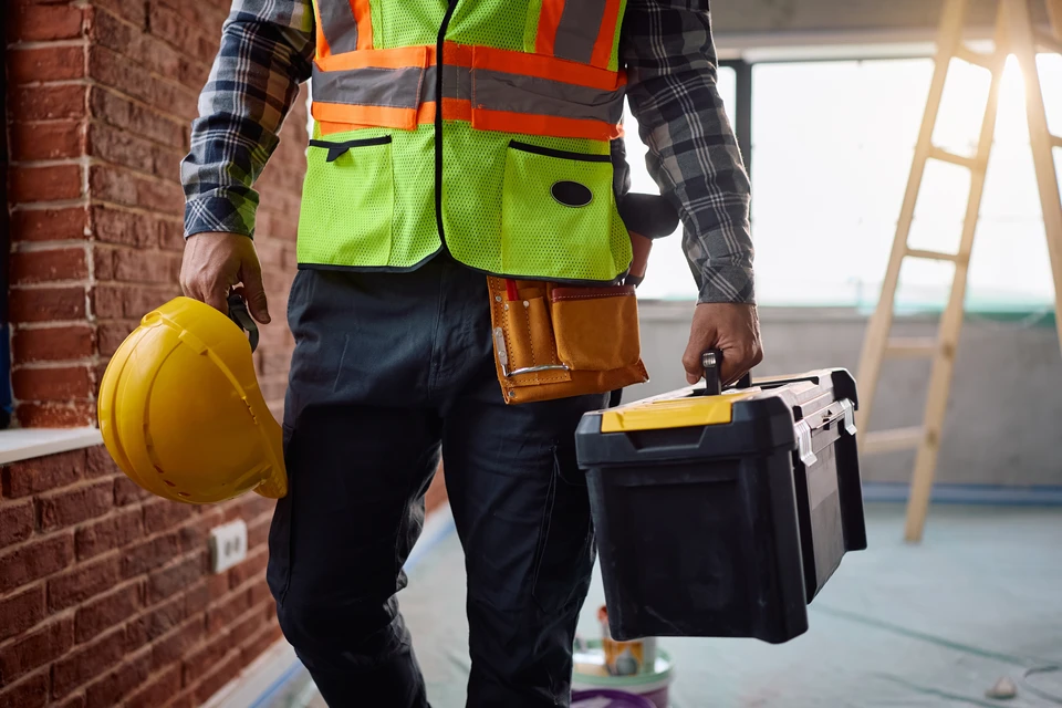 Chantier de construction intérieur avec ouvriers en arrière-plan portant casques de sécurité, travaillant dans un espace résidentiel en rénovation