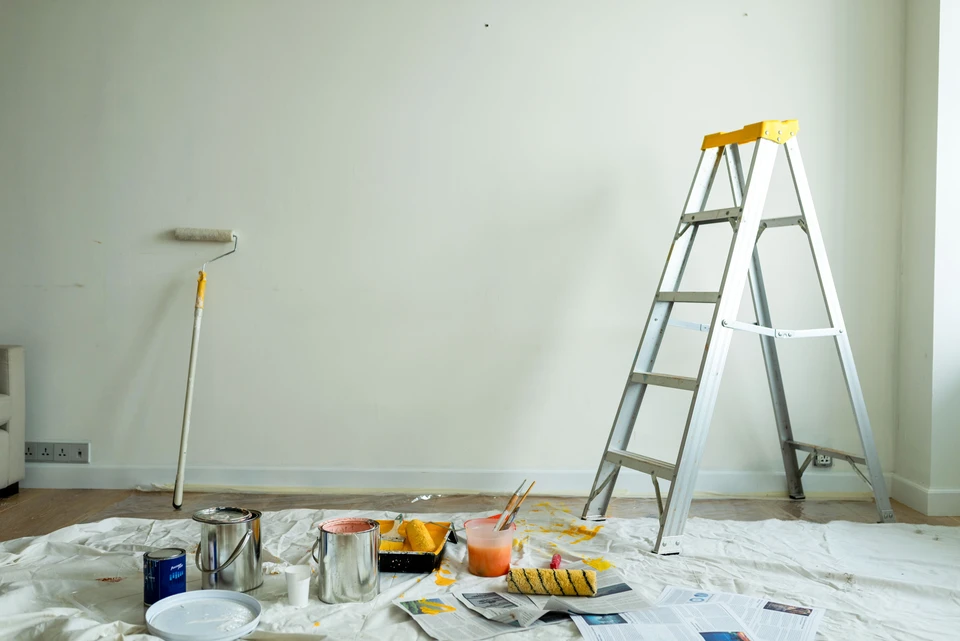 Artisan en vêtements de travail blancs applique de la peinture blanche sur un mur intérieur à l'aide d'un pinceau