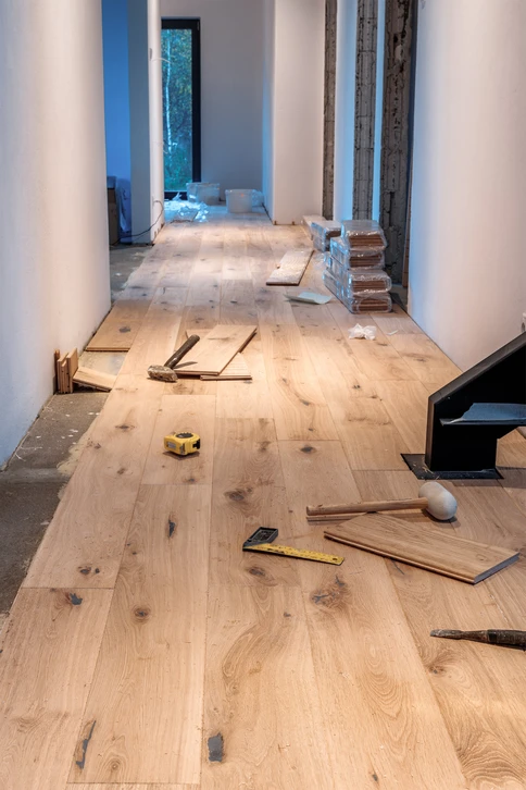 Intérieur d'habitation où un artisan en gants blancs installe du parquet flottant sur sous-couche